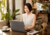 Woman works on a laptop with headphones in a sunny café.